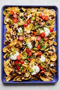 sloppy joe nachos on a baking sheet made with fritos topped with sloppy joe filling, cheese, black beans, and sour cream