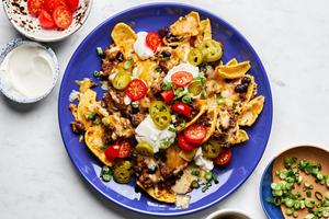 a plate of sloppy joe nachos made with fritos topped with sloppy joe filling, cheese, black beans, tomatoes and sour cream