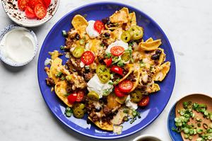 a plate of sloppy joe nachos made with fritos topped with sloppy joe filling, cheese, black beans, tomatoes and sour cream
