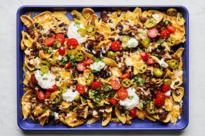 sloppy joe nachos on a baking sheet made with fritos topped with sloppy joe filling, cheese, black beans, and sour cream