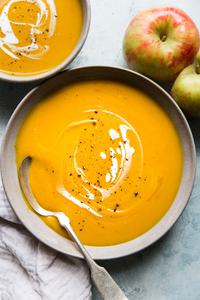 two bowls of slow cooker butternut squash apple soup with a coconut milk drizzle on top