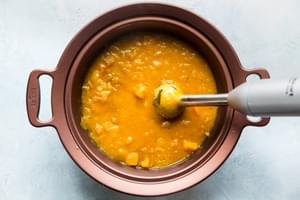 slow cooker butternut squash soup in a slow-cooker being blended with an immersion blender