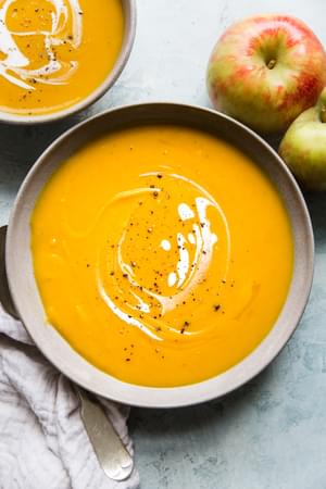 two bowls of butternut squash soup with apples topped with coconut cream and freshly cracked pepper