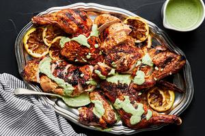 spatchcocked grilled chicken on a serving platter drizzled with homemade herb sauce