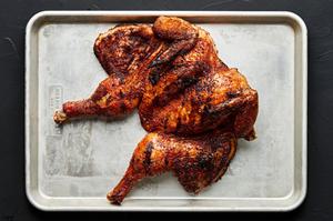 a grilled spatchcocked chicken seasoned with brown sugar, paprika, garlic powder, pepper and salt resting on a baking sheet
