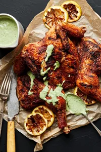 Spatchcocked Grilled Chicken on parchment paper drizzled with homemade herb sauce