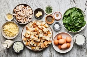 cubed bread, onion, mushrooms, spinach, Swiss cheese, eggs, milk, cream, spices and dijon in prep bowl to make strata