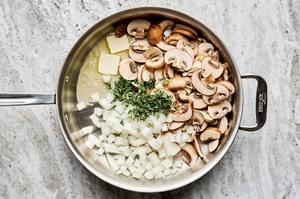 sliced onion, sliced mushrooms, and thyme being cooked in melted butter in a skillet
