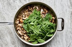 spinach being added to a pan with sliced onion, sliced mushrooms, thyme and butter