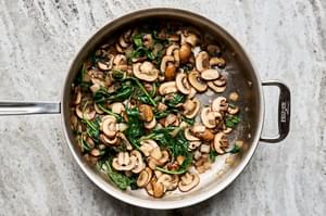 spinach, onion, mushrooms, thyme and butter being cooked in a skillet