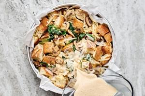 blended egg and spice mixture being poured over toasted bread, swiss cheese and vegetables in a baking pan