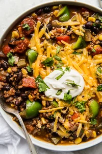 a bowl of homemade taco soup made with ground beef and black beans topped with cheddar cheese, sour cream and fresh cilantro