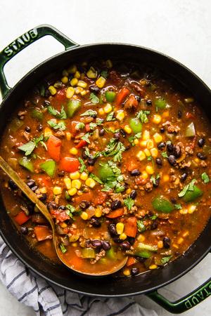 a pot of homemade taco soup made with ground beef, black beans, corn and bell pepper being scooped with a ladle