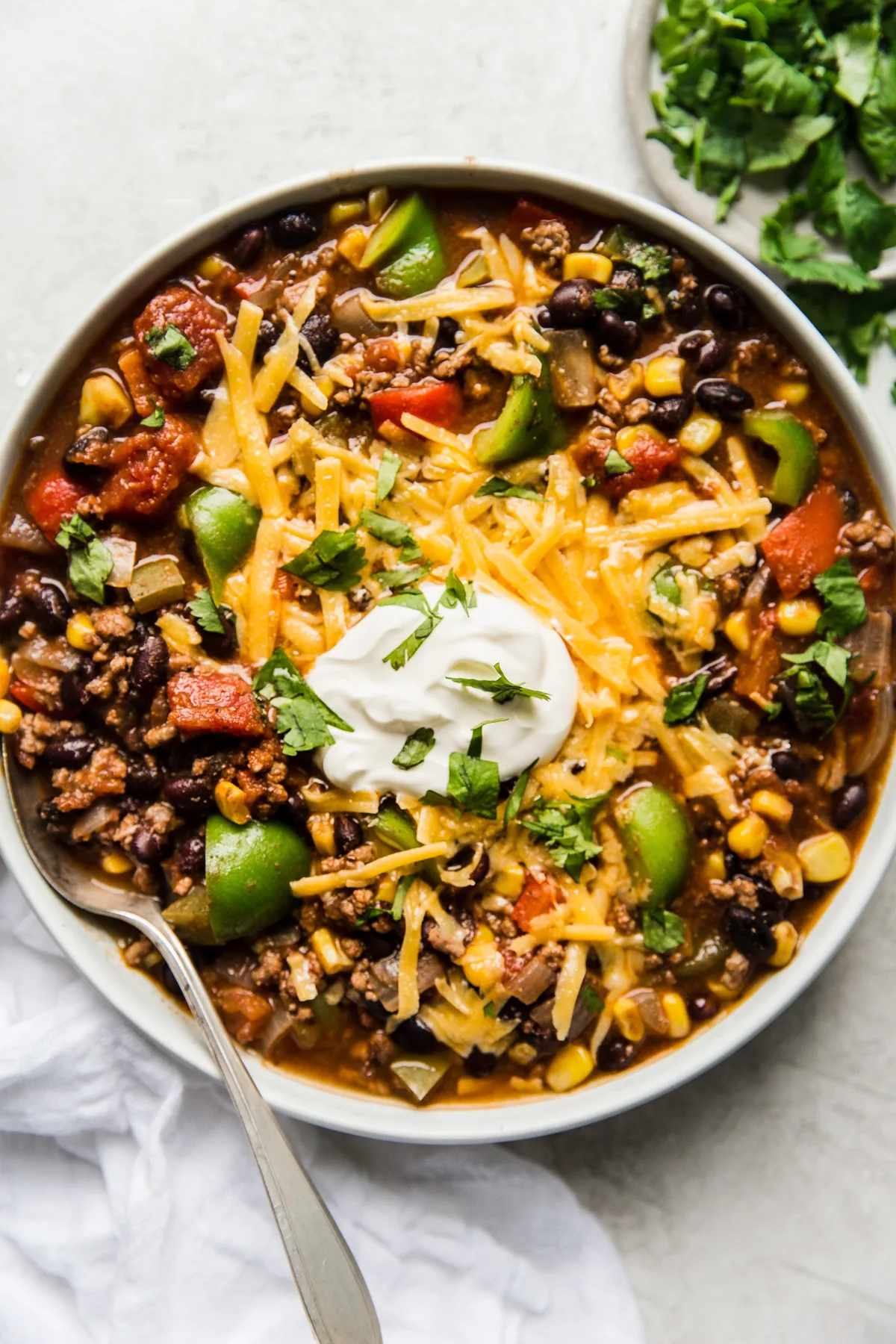 a bowl of homemade taco soup made with ground beef and black beans topped with cheddar cheese, sour cream and fresh cilantro