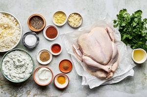 Ingredients for tandoori chicken: vibrant spices, yogurt, garlic, cilantro, pita bread and raita laid out in bowls
