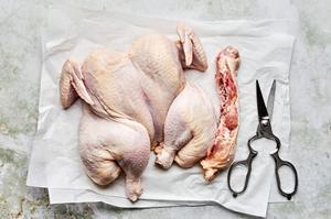 the spine of a raw chicken being cut out on top of parchment paper