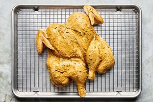 a whole chicken marinated with yogurt and vibrant spices on a rack lined baking sheet