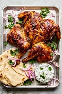 A whole roasted tandoori chicken served with warm pita bread and a side of creamy raita for dipping.