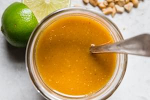 Glass jar with Thai salad dressing along with crushed peanuts and sliced limes