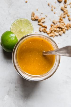 Glass jar with Thai salad dressing along with crushed peanuts and sliced limes