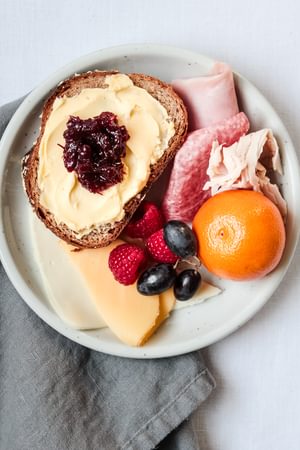 small plate of bread with butter and jam, cold meats and fresh fruit for an easy breakfast