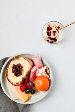 yogurt with pomegranate seeds in a small bowl next to a small plate of whole wheat bread with butter and jam