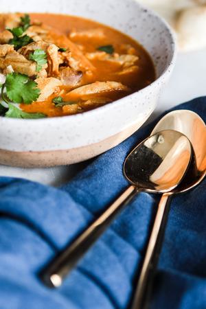 bowl of tikka masala soup with a linen and two gold spoons