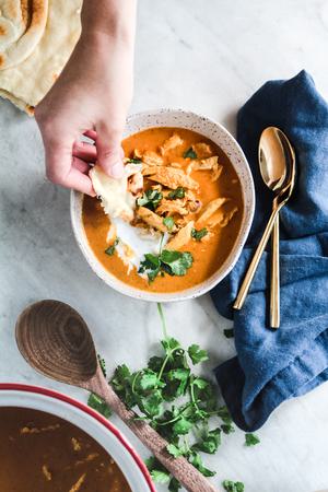 hand dipping fresh naan into a bowl of healthy tikka masala soup