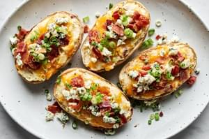 a platter of twice baked potatoes topped with cheddar, blue cheese, bacon and green onion