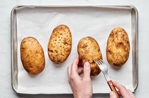 washed potatoes being priced with a fork on a parchment lined baking sheet