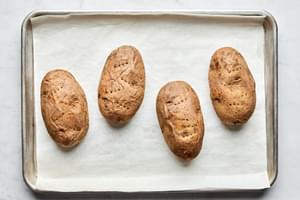4 baked potatoes on a parchment lined baking sheet