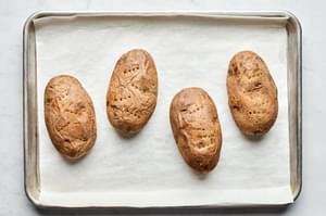 4 baked potatoes on a parchment lined baking sheet