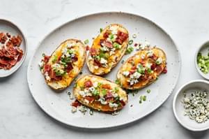 a platter of twice baked potatoes topped with cheddar, blue cheese, bacon and green onion