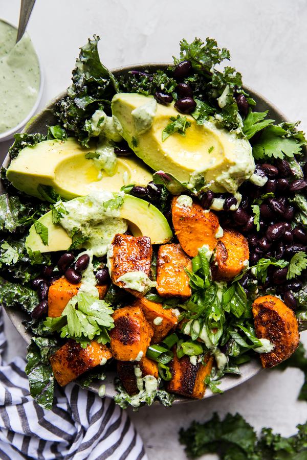 vegan roasted sweet potato and kale salad with black beans and avocado in a bowl with cashew cilantro dressing