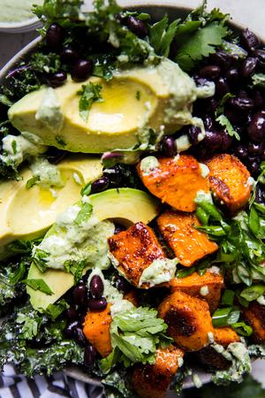 vegan roasted sweet potato and kale salad with black beans and avocado in a bowl with cashew cilantro dressing