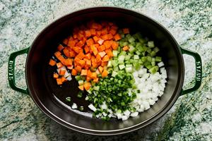 onion, celery, carrots, and jalapeño being cooked in olive oil in a dutch oven
