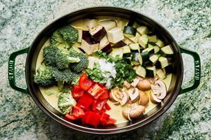 all ingredients for vegetable curry soup cooking in a pot including broccoli, eggplant, zucchini and bell pepper