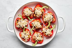 Vegetarian stuffed bell peppers filled with beans and rice topped with pepper jack cheese ready for the oven