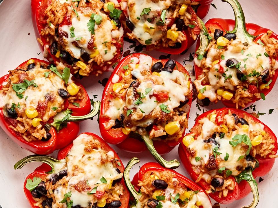 Vegetarian stuffed bell peppers in a casserole dish, topped with melted pepper jack cheese and garnished with cilantro