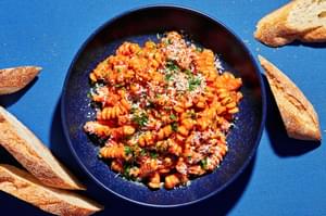 vodka sauce carbonara on cooked pasta topped with parmesan, parsley & red pepper flakes surrounded by sliced crusty bread