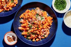 vodka sauce carbonara on cooked pasta topped with parmesan, parsley & red pepper flakes next to bowl of extra toppings