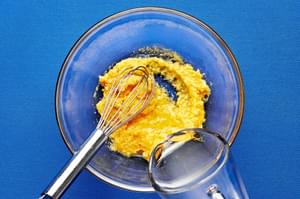 reserved pasta water being poured into a glass bowl with whisked eggs and parmesan cheese