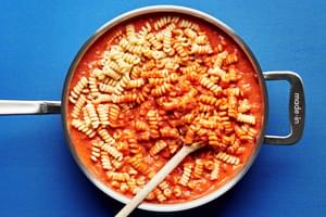 cooked pasta being stirred together with homemade vodka sauce carbonara in a sauce pan