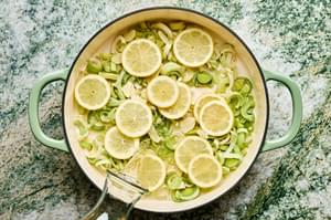 leeks, lemon slices, olive oil and wine layered on the bottom of a pan