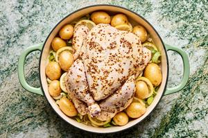 a whole chicken covered in spices on top of leeks and lemon slices and surrounded with potatoes in a pan
