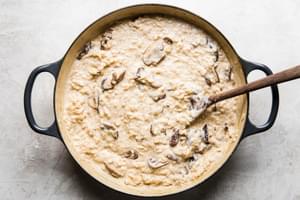 cooked mushrooms and shallot, Parmesan and heavy cream being stirred into risotto in a pot