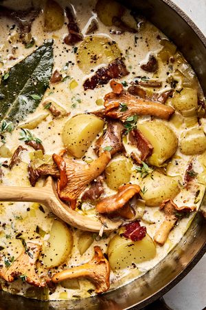 A pot of creamy wild mushroom chowder with bacon and leeks, topped with cracked black pepper and fresh thyme.