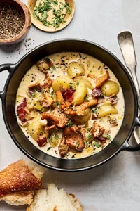 A bowl of creamy wild mushroom chowder with bacon and leeks, topped with cracked black pepper and fresh thyme.