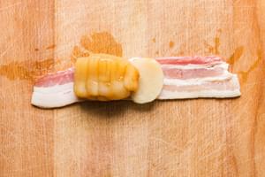 bacon strip on a cutting board with a marinated sea scallop and a water chestnut slice