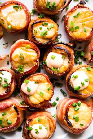 bacon wrapped scallops on a white plate topped with sriracha aioli and fresh chives